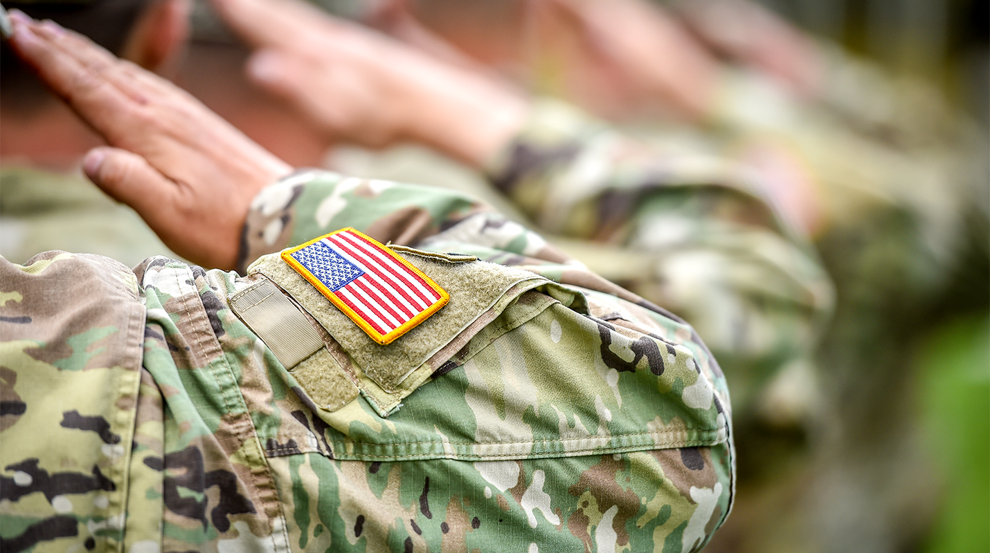 Military solders with American flag arm patch saluting. 