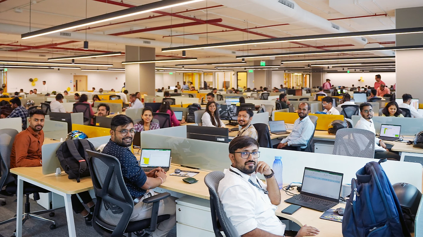 Group of employees at HYMH India facility smiling at their workstations.
