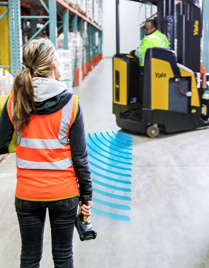 Woman in warehouse approaching Yale reach truck equipped with Yale Reliant operator assistance technology. 