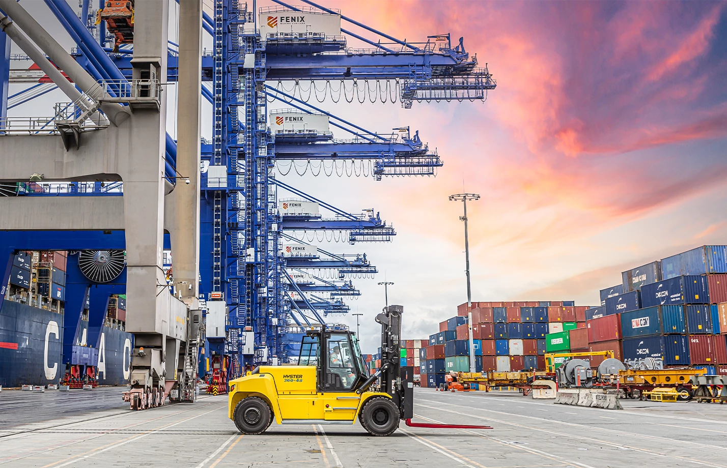 Operator driving a Hyster high-capacity forklift at a cargo port.